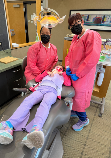 Dental team member and dentist treating dental patient observed by parent
